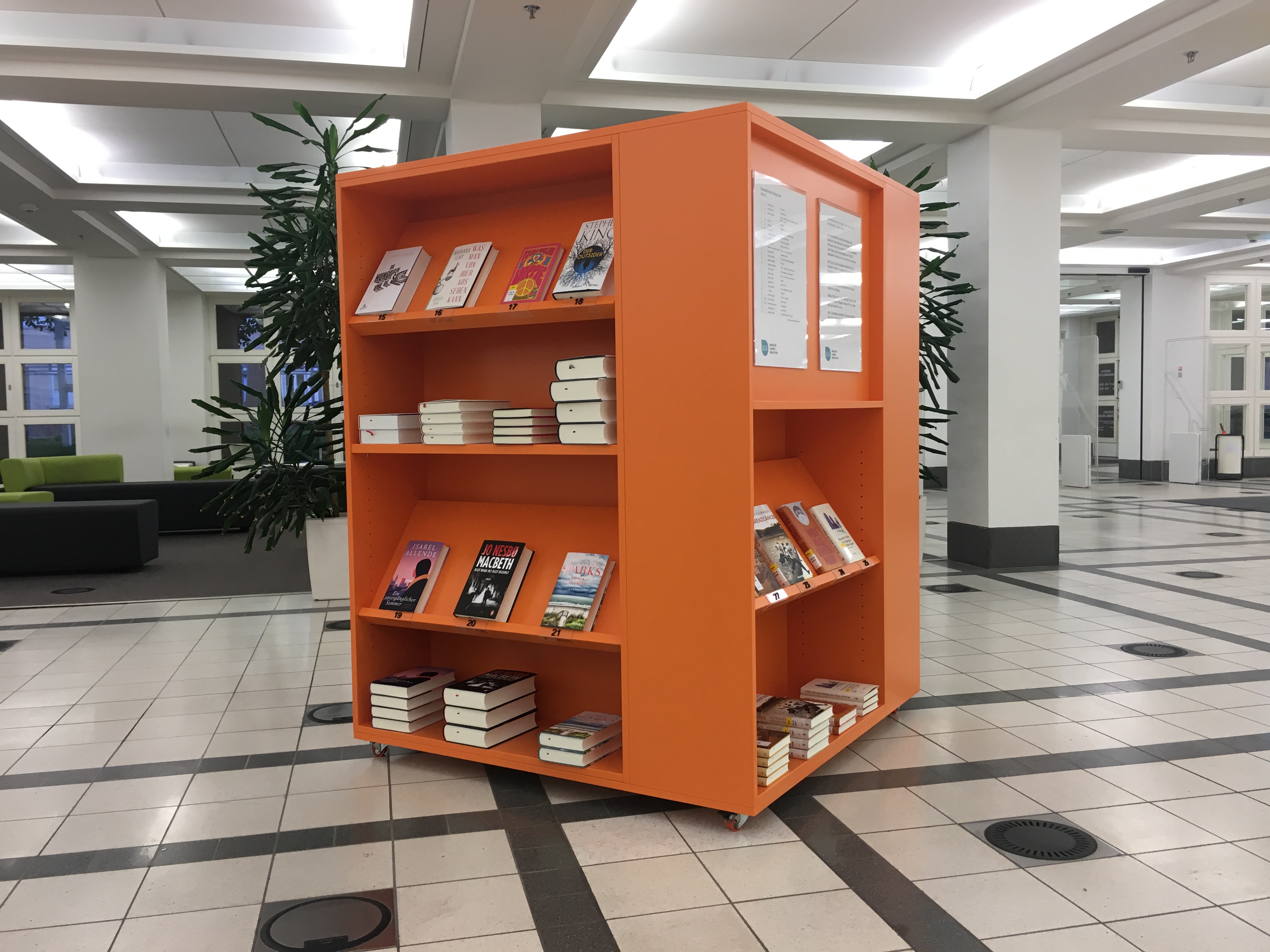 Zu sehen ist das orangene Bestsellerbücherregal im Foyer der BLB. 