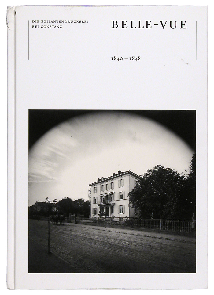 Zu sehen ist das weiße Cover eines Ausstellungskataloges, auf welchem klein im oberen Bildbereich der Titel der Ausstellung steht. Außerdem ist ein schwarz weiß Foto eines Gebäudes im unteren Bildbereich abgebildet.