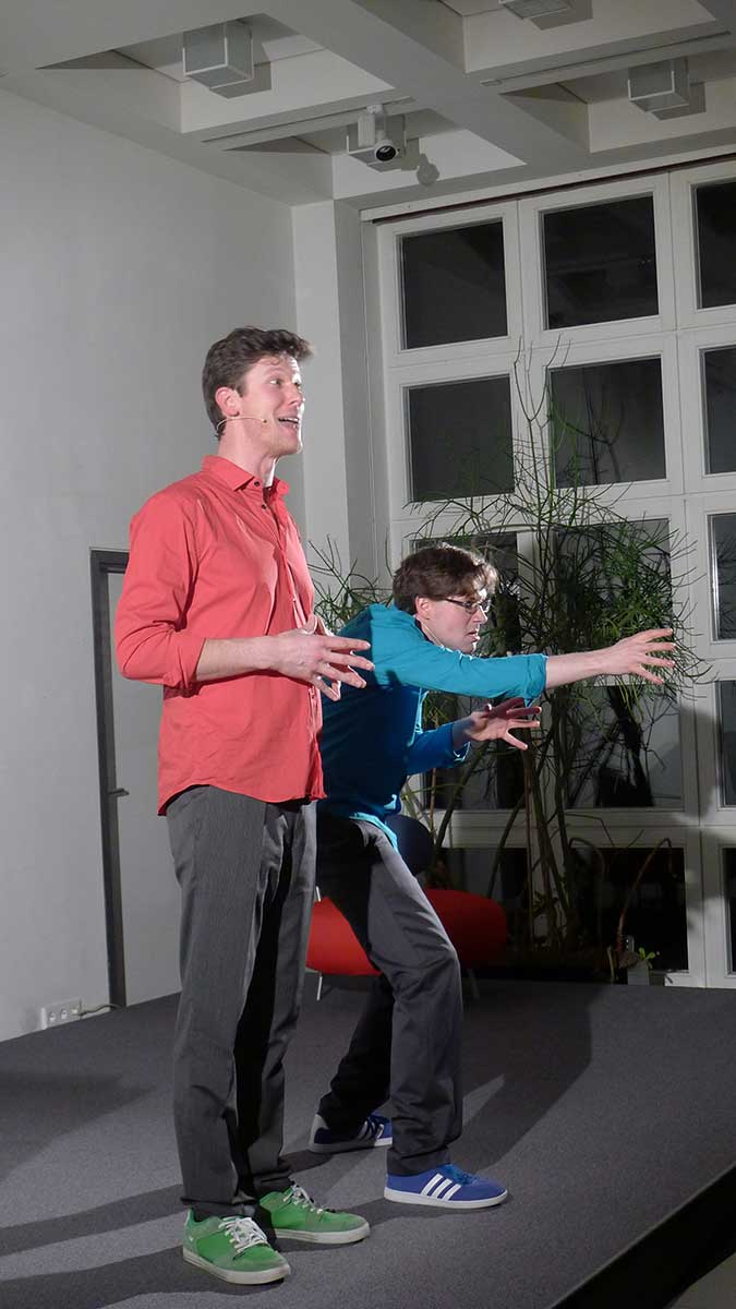 Das Foto zeigt lebendige Bühnenpoesie oder Geschichtenerzählen mit Ganzkörpereinsatz von Jakob Nacken (links) und Harry Kienzler (rechts).