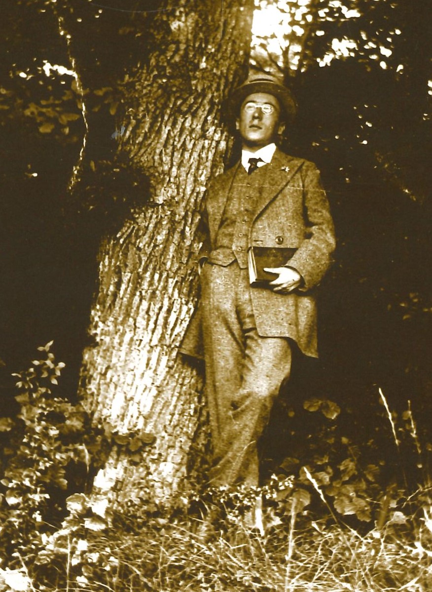 Die Fotografie zeigt Lautenschlager als jungen Mann im Anzug und mit Hut, mit der rechten Seite an einen Baum gelehnt, mit der linken Hand ein Buch haltend.