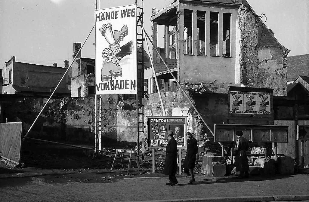 Zu sehen ist auf dem Schwarz-Weiß-Foto eine Bauruine, davor ein großes Banner mit der Aufschrift „Hände weg von Baden“. Passanten gehen davor vorbei.
