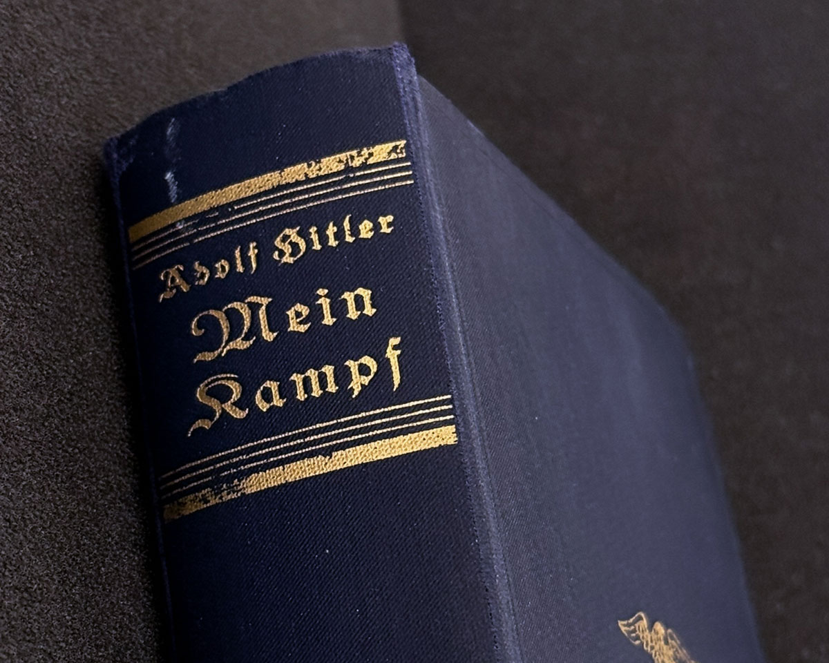 Buchrücken einer historischen Ausgabe von „Mein Kampf“ mit dunkelblauem Ledereinband und goldener Schrift für Titel und Autor.