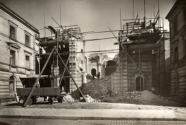 Auf dem Foto ist eine Ruine zu sehen. Schutt türmt sich im Inneren, der obere Gebäudeteil fehlt. An der Fassade zur Straßenseite ist ein provisorisches Gerüst angebracht.