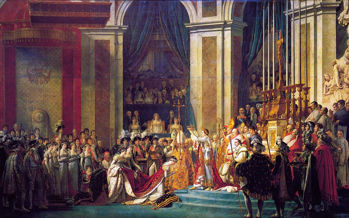 In einer großen, prunkvollen Halle hebt Napoleon eine Krone über den Kopf seiner Frau Joséphine. Um sie herum stehen zahlreiche festlich gekleidete Würdenträger.