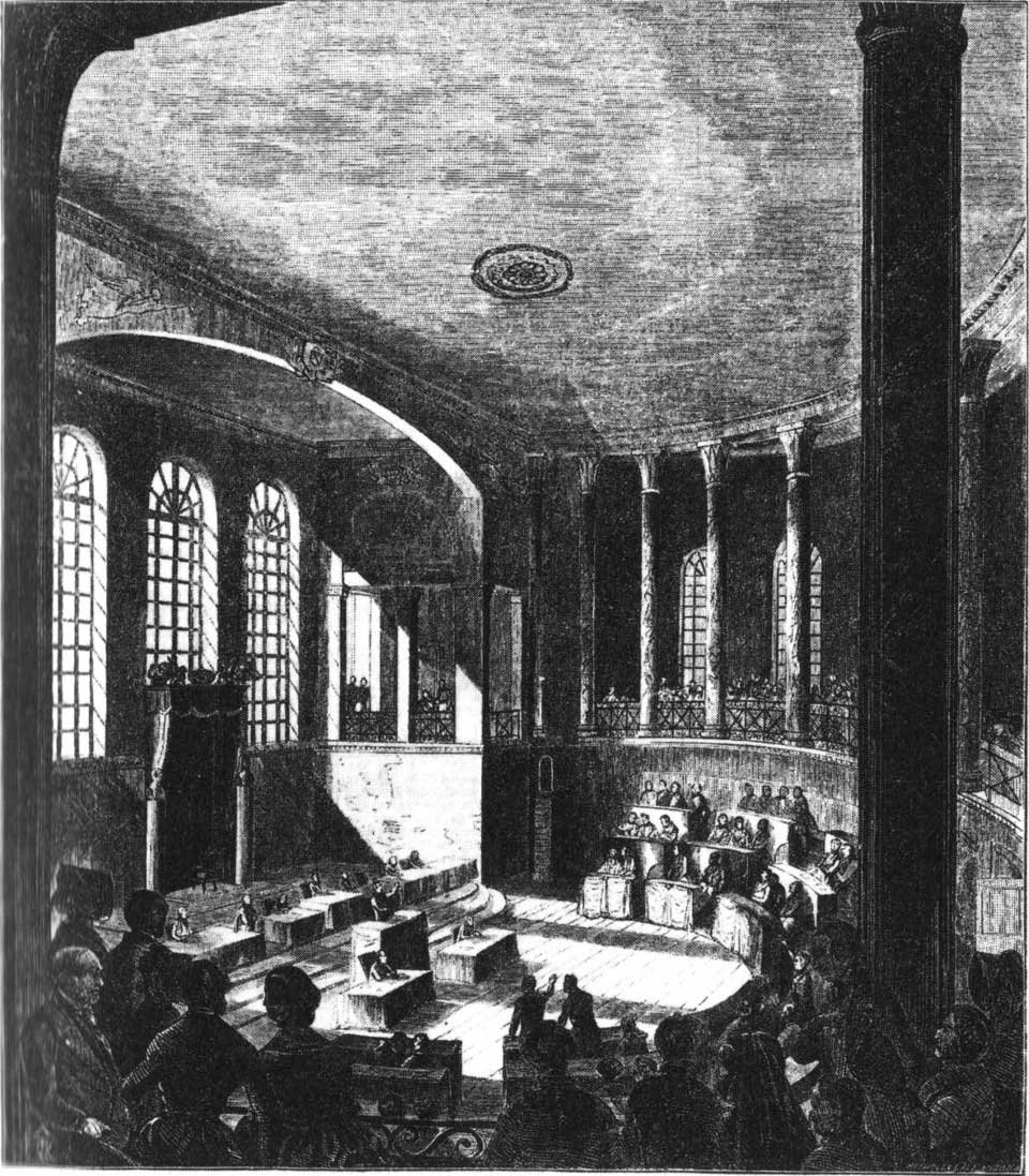 Schwarz-weiße Innenansicht eines historischen Versammlungssaals mit hohen Fenstern, Säulen und mehreren Personen an Tischen und auf einer erhöhten Galerie.