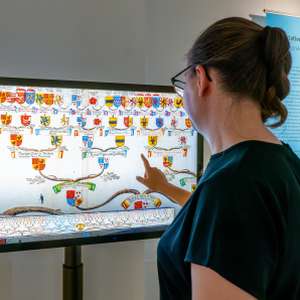 Eine junge Frau steht vor einem Touchscreen, auf dem ein Stammbaum zu sehen ist.