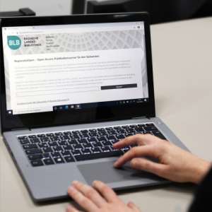 An einem Laptop arbeitende Hände, auf dem Monitor ist die Webseite von RegionaliaOpen zu sehen