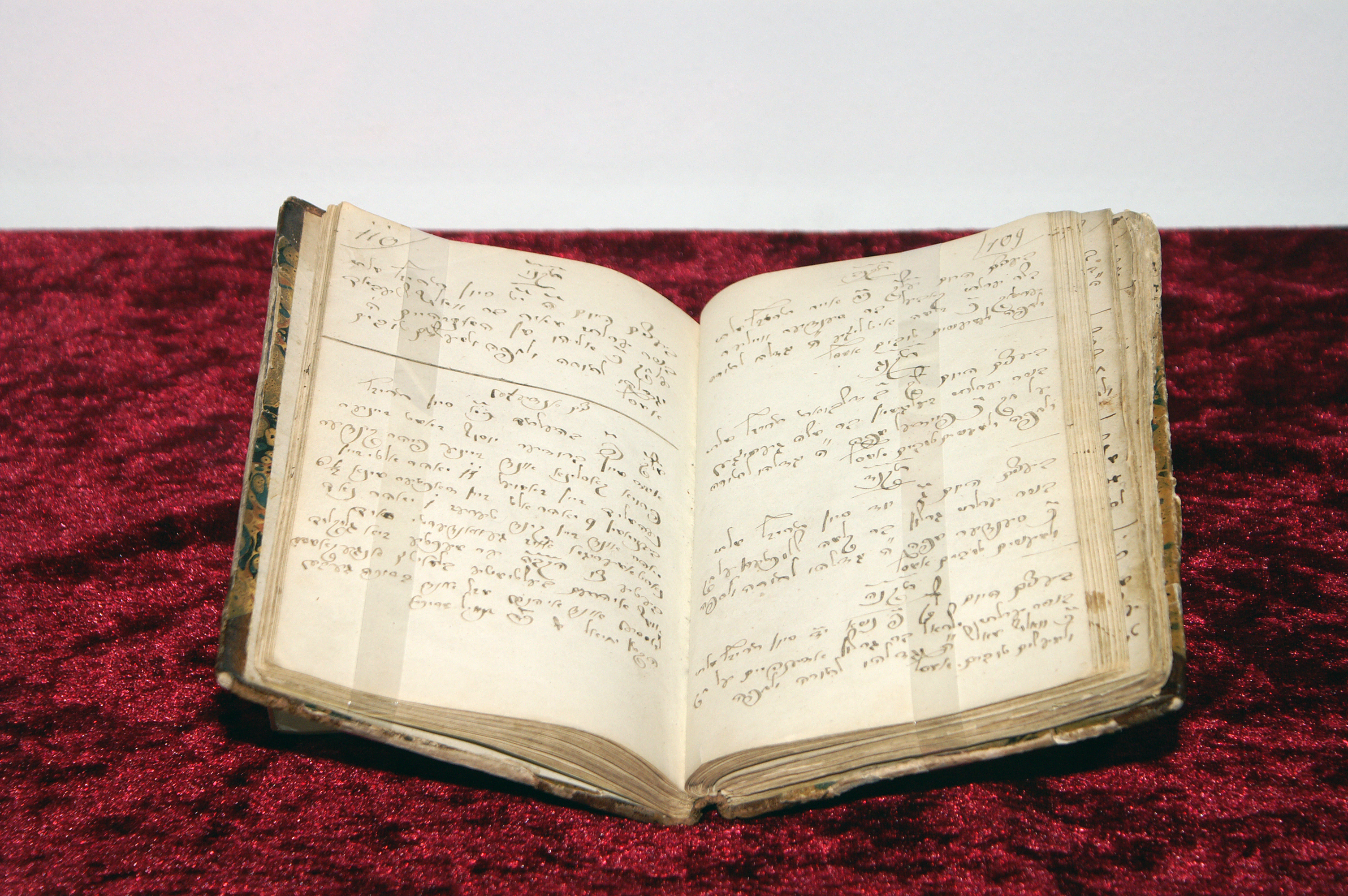 Das Notizbuch des Mohel Jehiel Schwarzschild liegt aufgeschlagen auf rotem Samtstoff. Die Schrift ist schön geschwungen und fein säuberlich.
