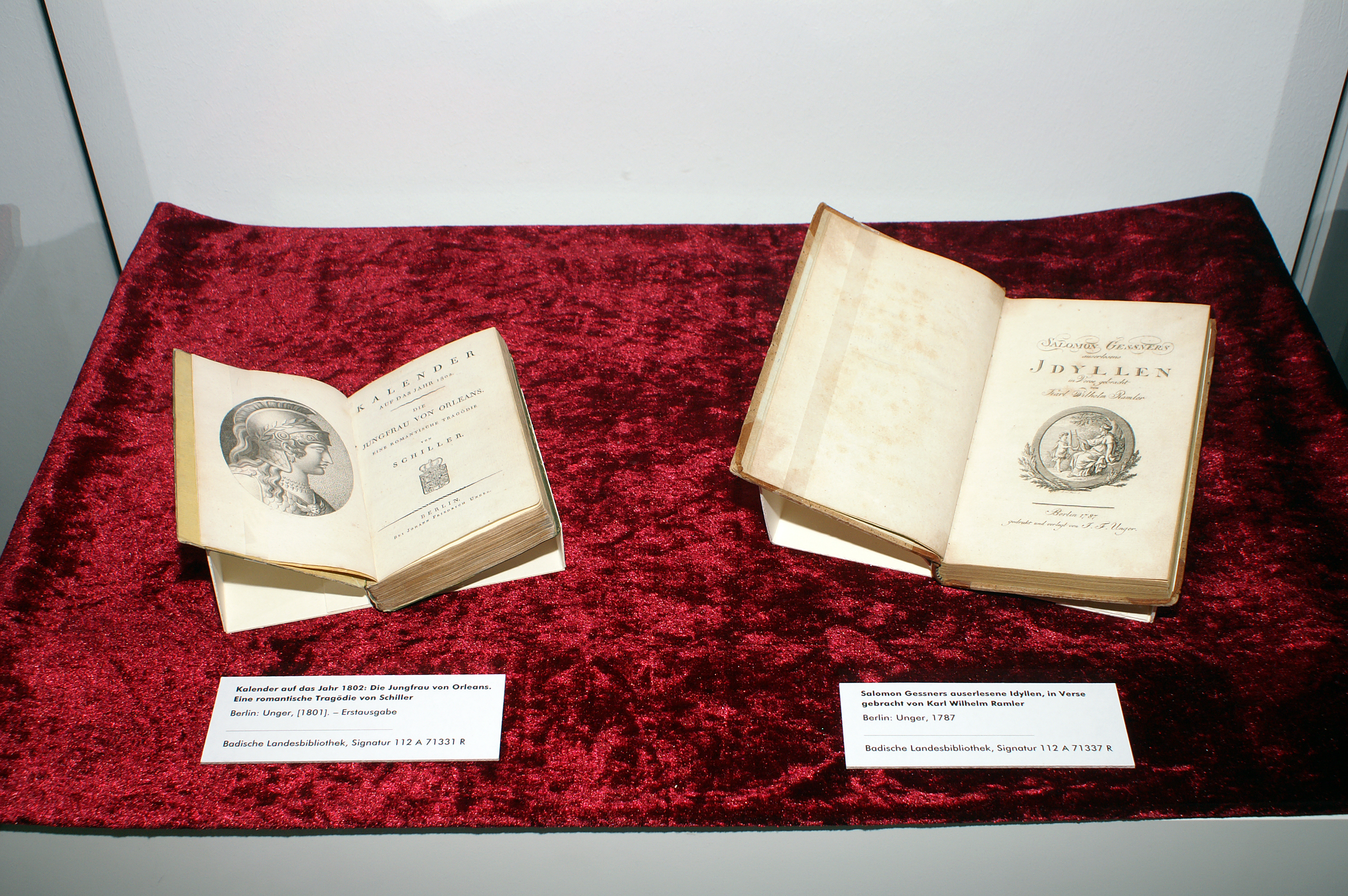 Aufgeschlagen auf rotem Samt liegt links der "Kalender auf das Jahr 1802: Die Jungfrau von Orleans" und rechts Salomon Gessners auserlesene "Idyllen".